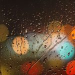 Close-up of raindrops on glass with blurred colorful city lights in the background.